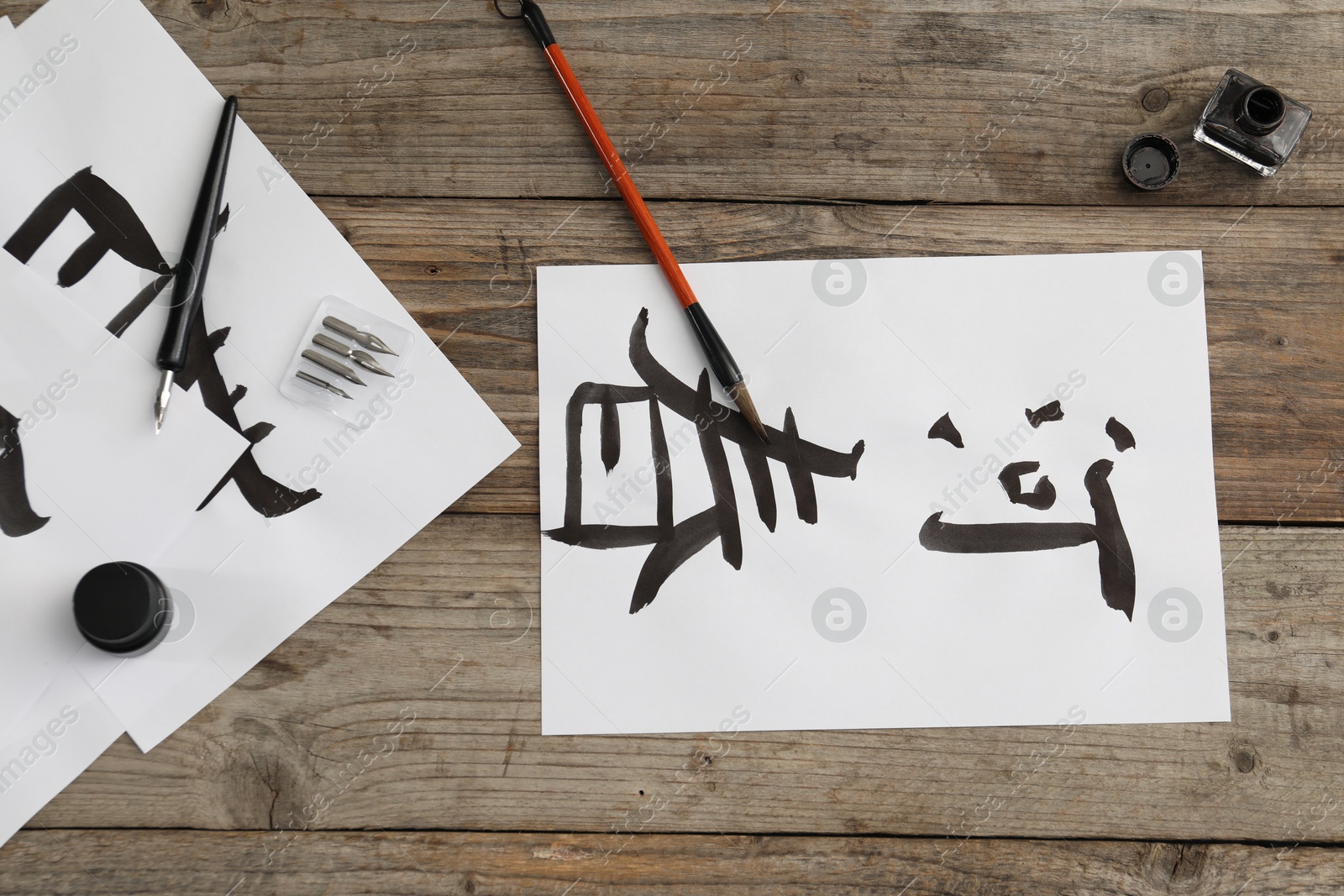 Photo of Calligraphy. Papers with written Chinese hieroglyphs, inkwell, fountain pen and brush on wooden table, flat lay