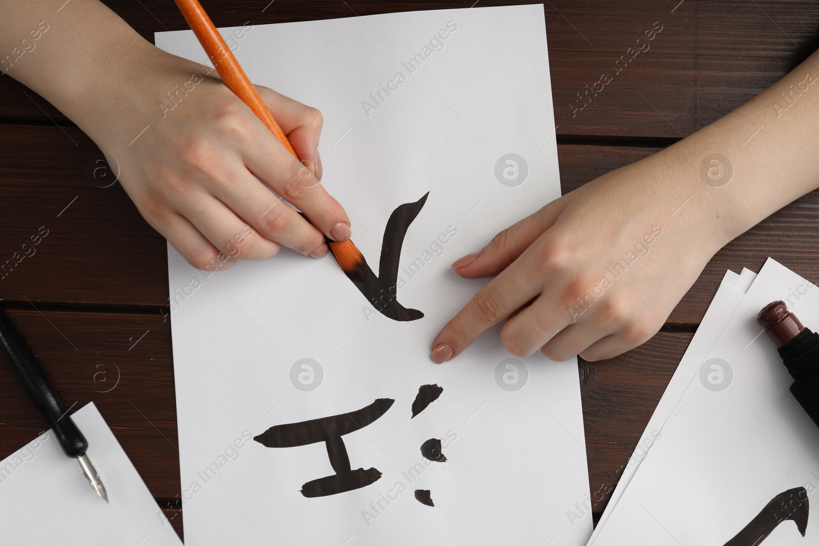 Photo of Calligraphy. Woman with brush writing words River and Entrance in Chinese on paper at wooden table, top view