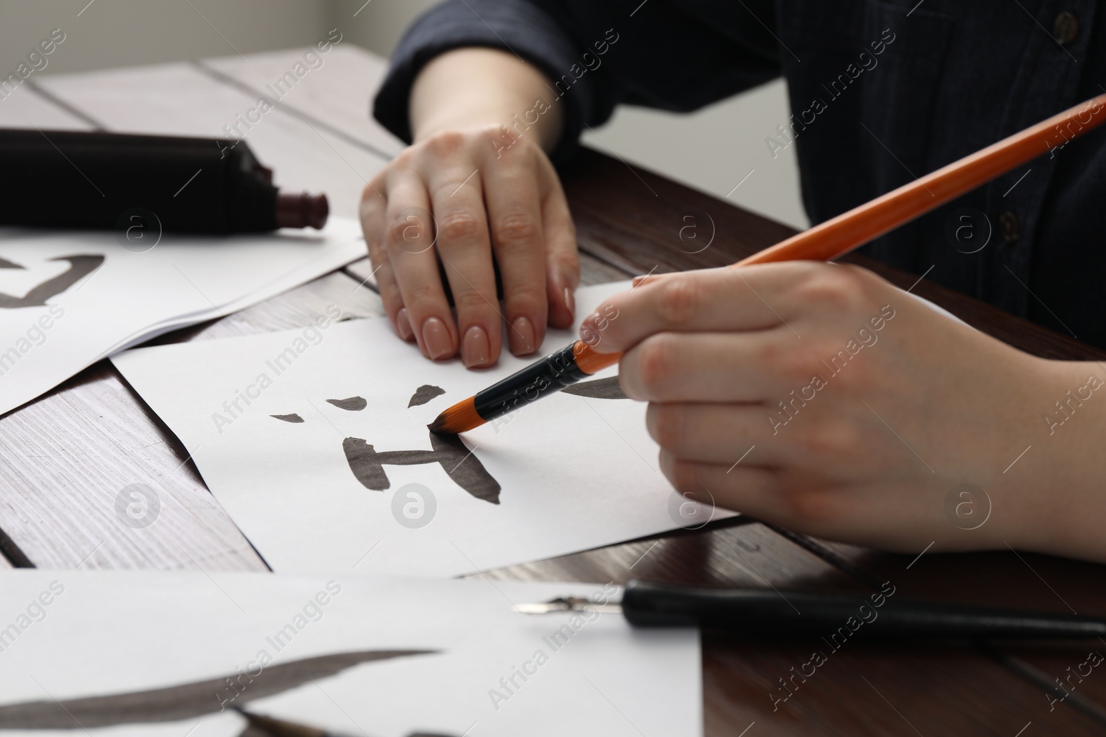 Photo of Calligraphy. Woman with brush writing word River in Chinese on paper at wooden table, closeup