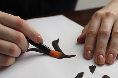 Photo of Calligraphy. Woman with brush writing word Entrance in Chinese on paper at table, closeup