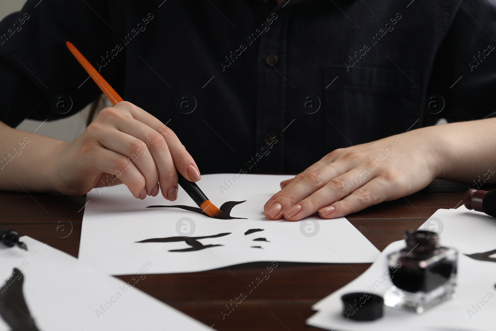 Photo of Calligraphy. Woman with brush and inkwell writing words River and Entrance in Chinese on paper at wooden table, closeup