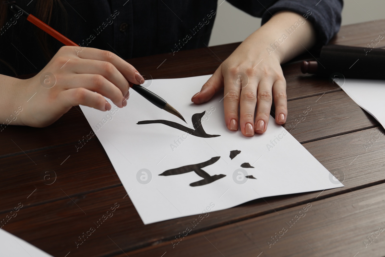 Photo of Calligraphy. Woman with brush writing words River and Entrance in Chinese on paper at wooden table, closeup