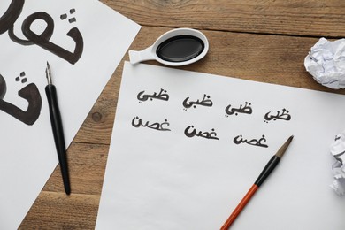 Calligraphy. Sheets of paper with written words Antilope and Branch in Arabian language, inkwell, fountain pen and brush on wooden table, flat lay