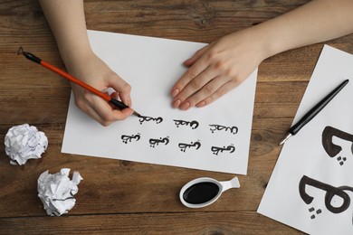 Calligraphy. Woman with brush writing words Antilope and Branch in Arabian language on paper at wooden table, top view