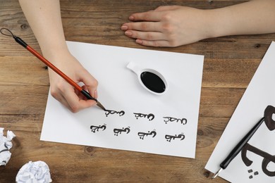 Calligraphy. Woman with brush writing words Antilope and Branch in Arabian language on paper at wooden table, top view