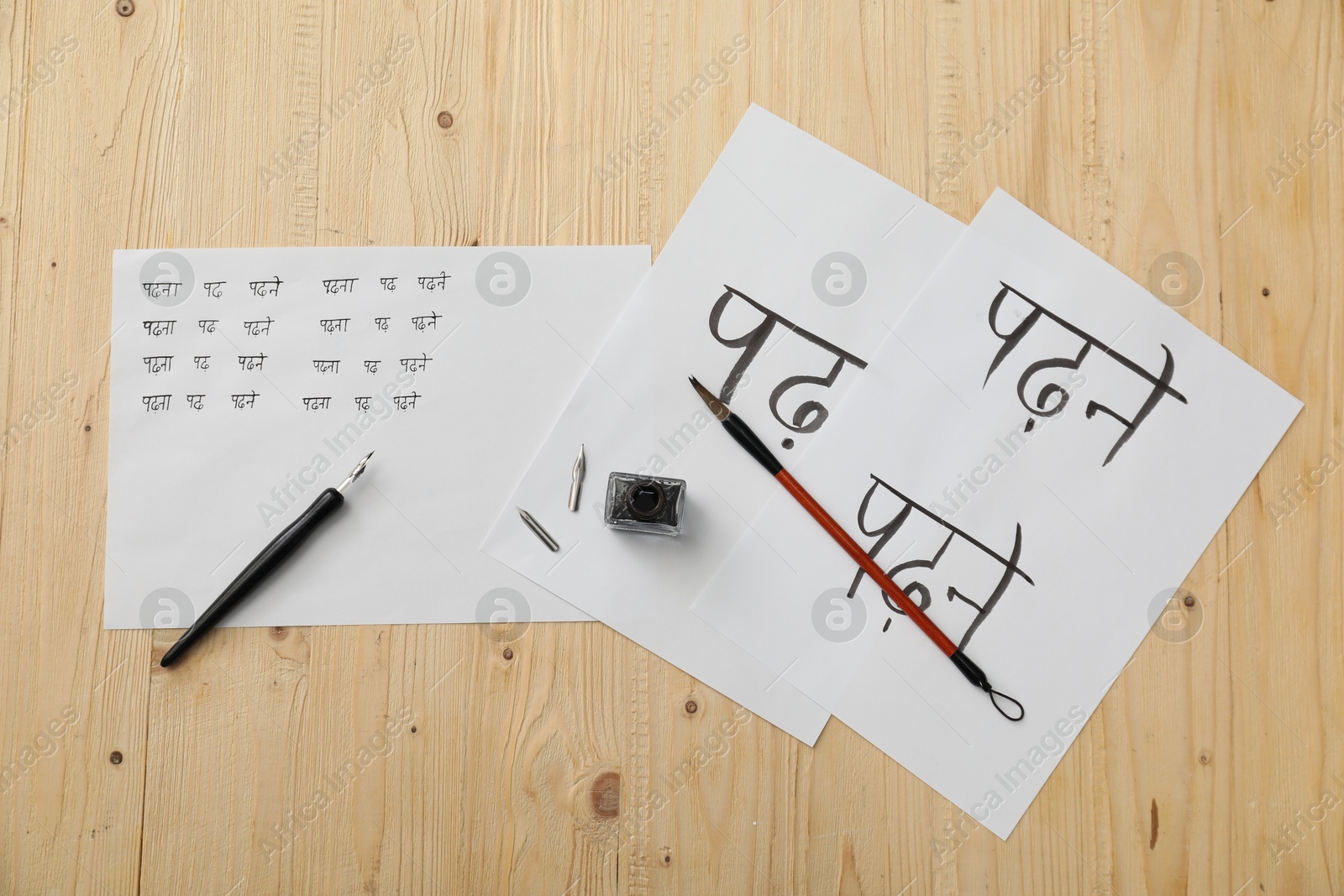 Photo of Calligraphy. Sheets of paper with written words Reading and Read in Hindi, inkwell, fountain pen and brush on wooden table, top view