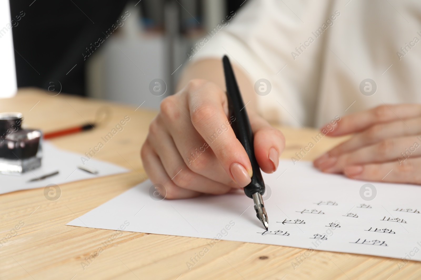 Photo of Calligraphy. Woman with fountain pen writing words Reading and Read in Hindi on paper at wooden table, closeup