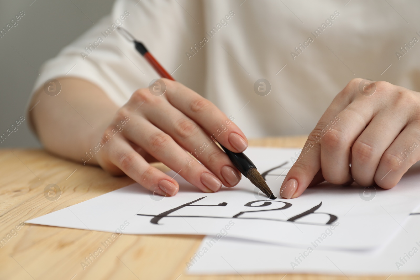 Photo of Calligraphy. Woman with brush writing word Reading in Hindi on paper at wooden table, closeup