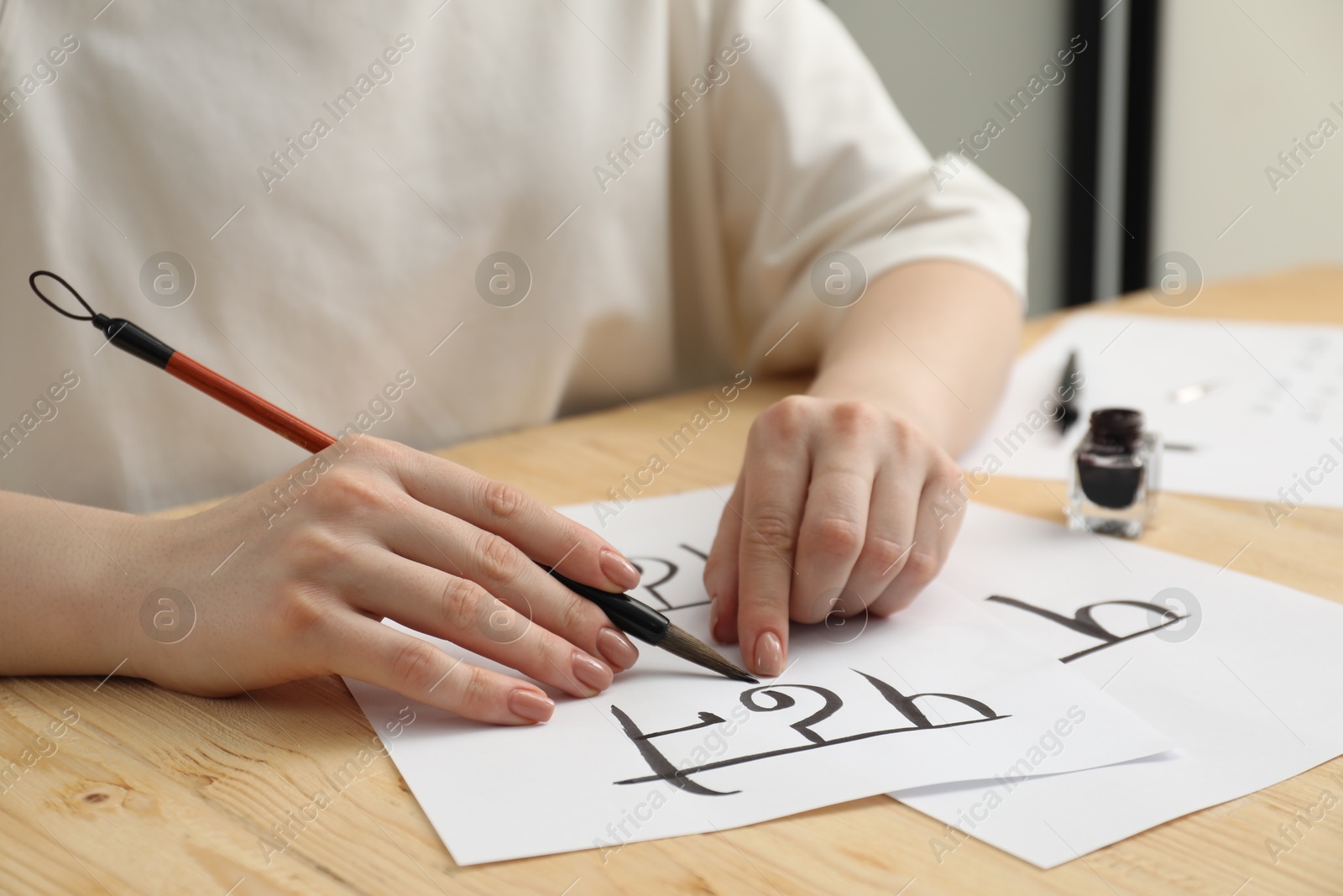 Photo of Calligraphy. Woman with brush writing word Reading in Hindi on paper at wooden table, closeup