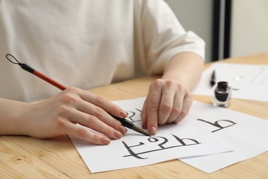 Calligraphy. Woman with brush writing word Reading in Hindi on paper at wooden table, closeup