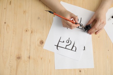 Calligraphy. Woman with brush writing words Reading and Read in Hindi on paper at wooden table, top view. Space for text