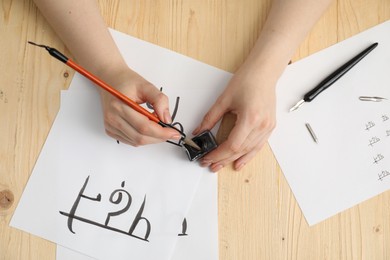 Calligraphy. Woman with brush writing words Reading and Read in Hindi on paper at wooden table, top view