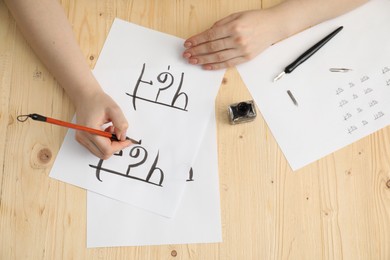 Photo of Calligraphy. Woman with brush writing words Reading and Read in Hindi on paper at wooden table, top view