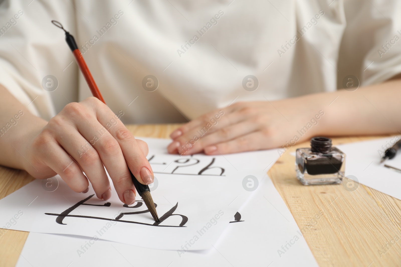 Photo of Calligraphy. Woman with brush writing words Reading and Read in Hindi on paper at wooden table, closeup