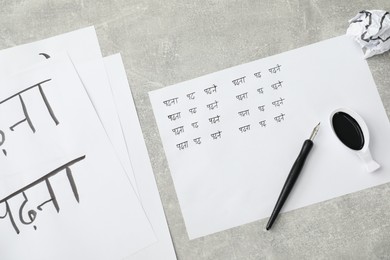 Photo of Calligraphy. Sheets of paper with written words Reading and Read in Hindi, inkwell and fountain pen on grey background, top view