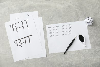 Calligraphy. Sheets of paper with written words Reading and Read in Hindi, inkwell and fountain pen on grey background, top view