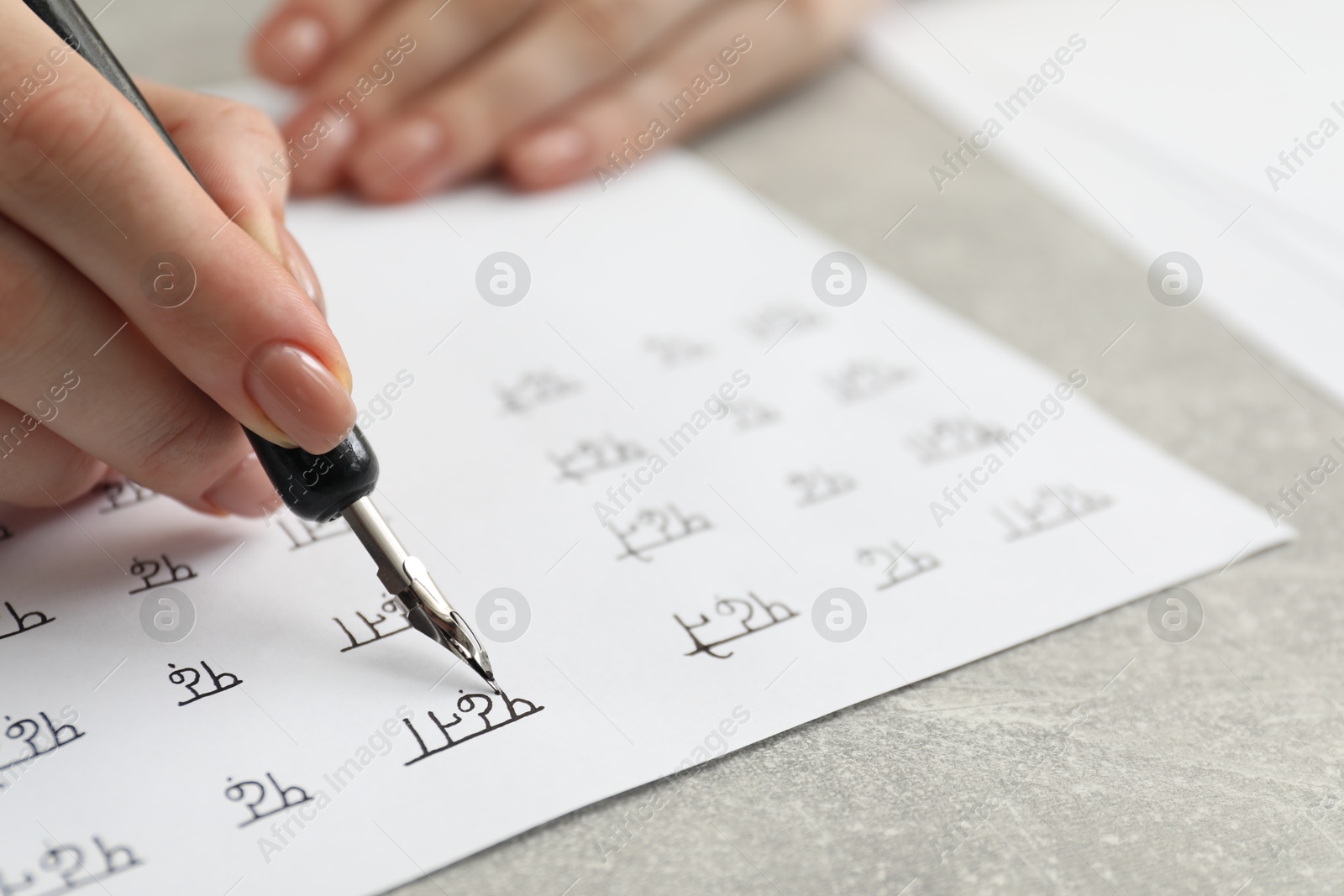 Photo of Calligraphy. Woman with fountain pen writing words Reading and Read in Hindi on paper at grey table, closeup