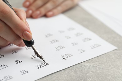 Calligraphy. Woman with fountain pen writing words Reading and Read in Hindi on paper at grey table, closeup