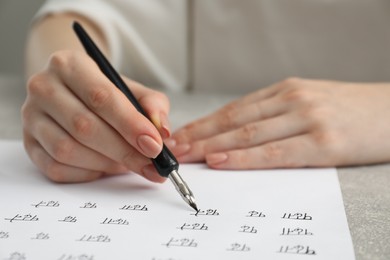 Photo of Calligraphy. Woman with fountain pen writing words Reading and Read in Hindi on paper at grey table, closeup