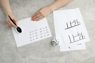 Photo of Calligraphy. Woman with fountain pen writing words Reading and Read in Hindi on paper at grey table, top view