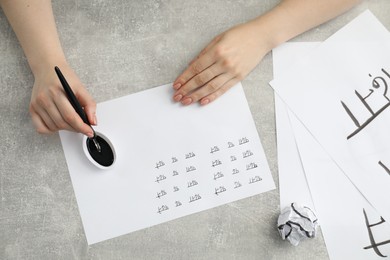 Photo of Calligraphy. Woman with fountain pen writing words Reading and Read in Hindi on paper at grey table, top view