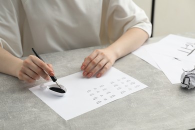 Photo of Calligraphy. Woman with fountain pen writing words Reading and Read in Hindi on paper at grey table, closeup