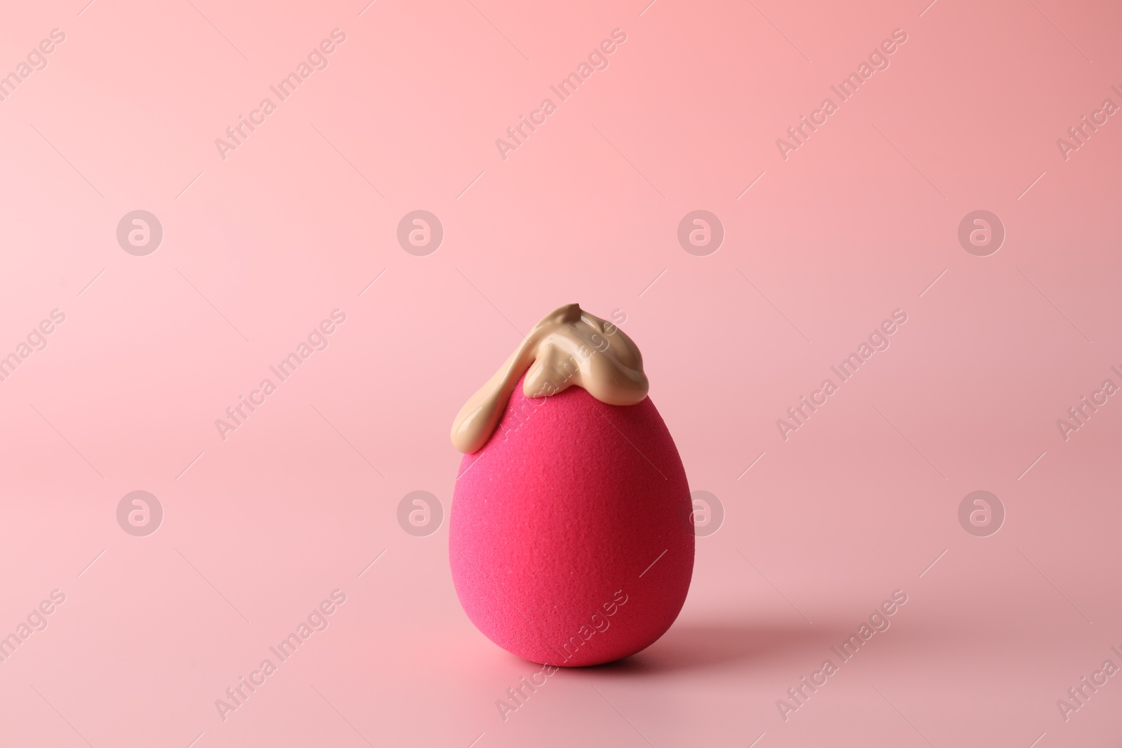 Photo of Makeup sponge with skin foundation on pink background