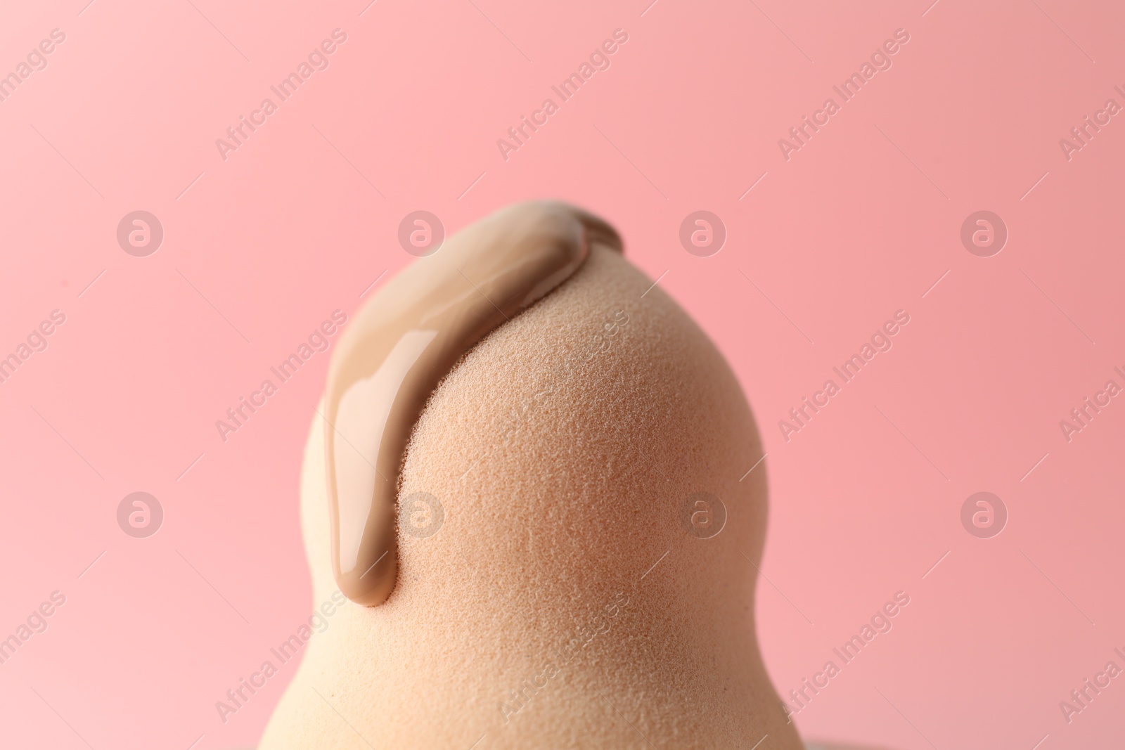 Photo of Makeup sponge with skin foundation on pink background, closeup