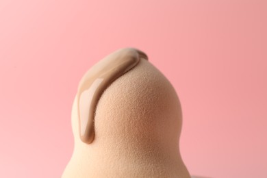 Photo of Makeup sponge with skin foundation on pink background, closeup