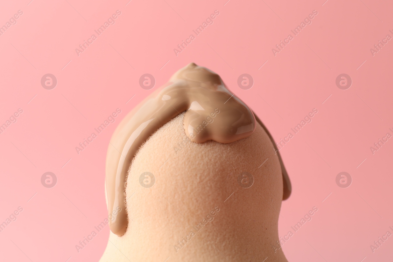 Photo of Makeup sponge with skin foundation on pink background, closeup