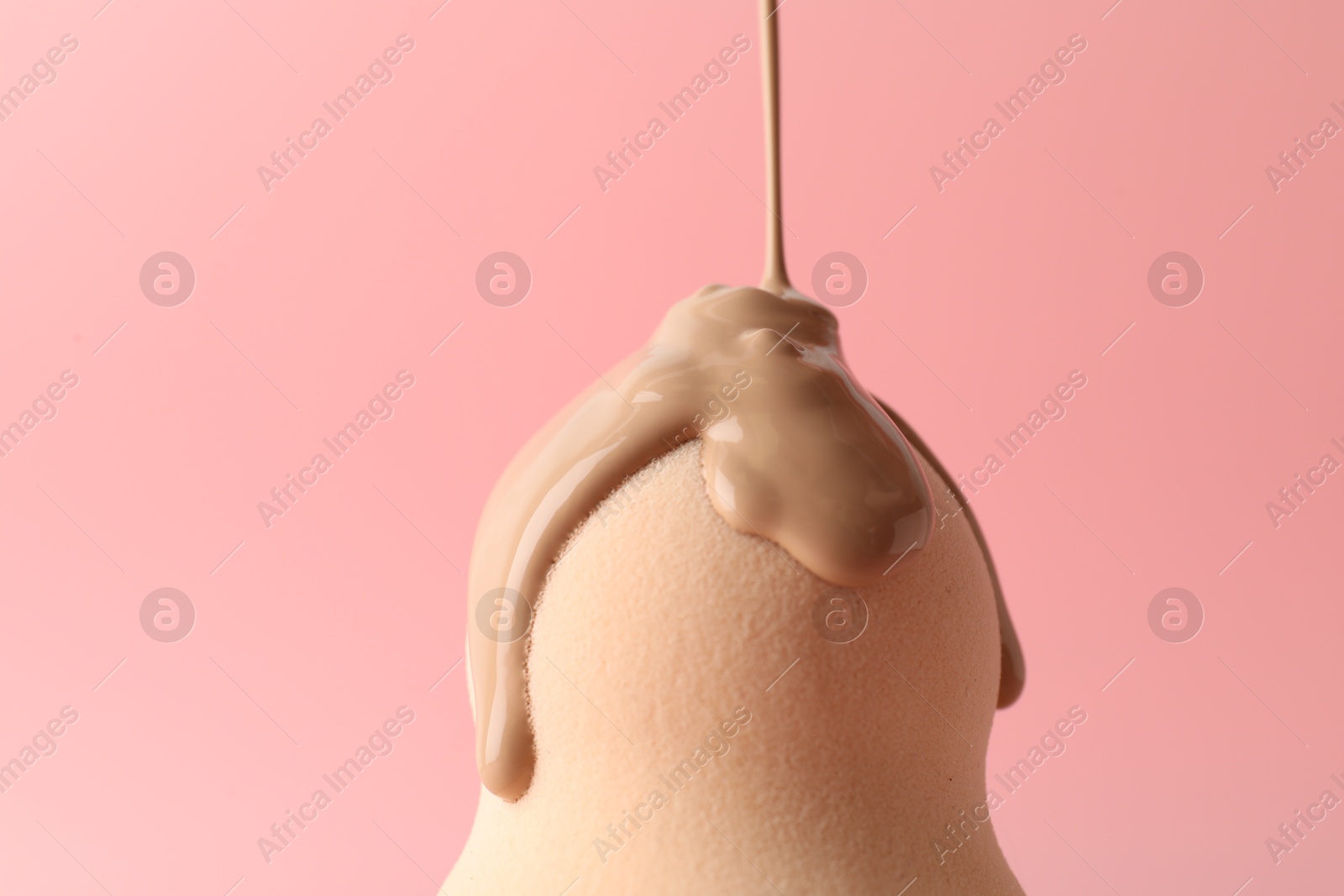 Photo of Pouring skin foundation onto makeup sponge against pink background, closeup