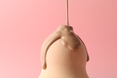 Photo of Pouring skin foundation onto makeup sponge against pink background, closeup