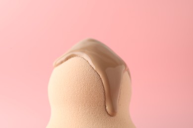 Photo of Makeup sponge with skin foundation on pink background, closeup