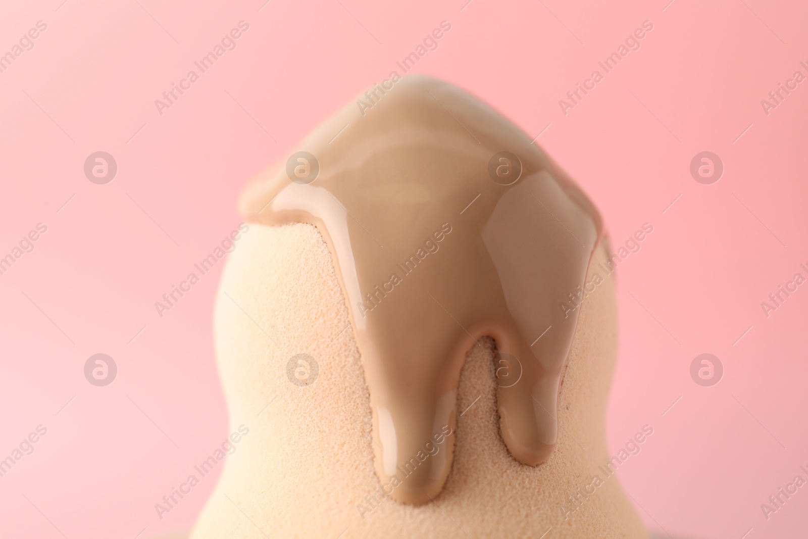 Photo of Makeup sponge with skin foundation on pink background, closeup