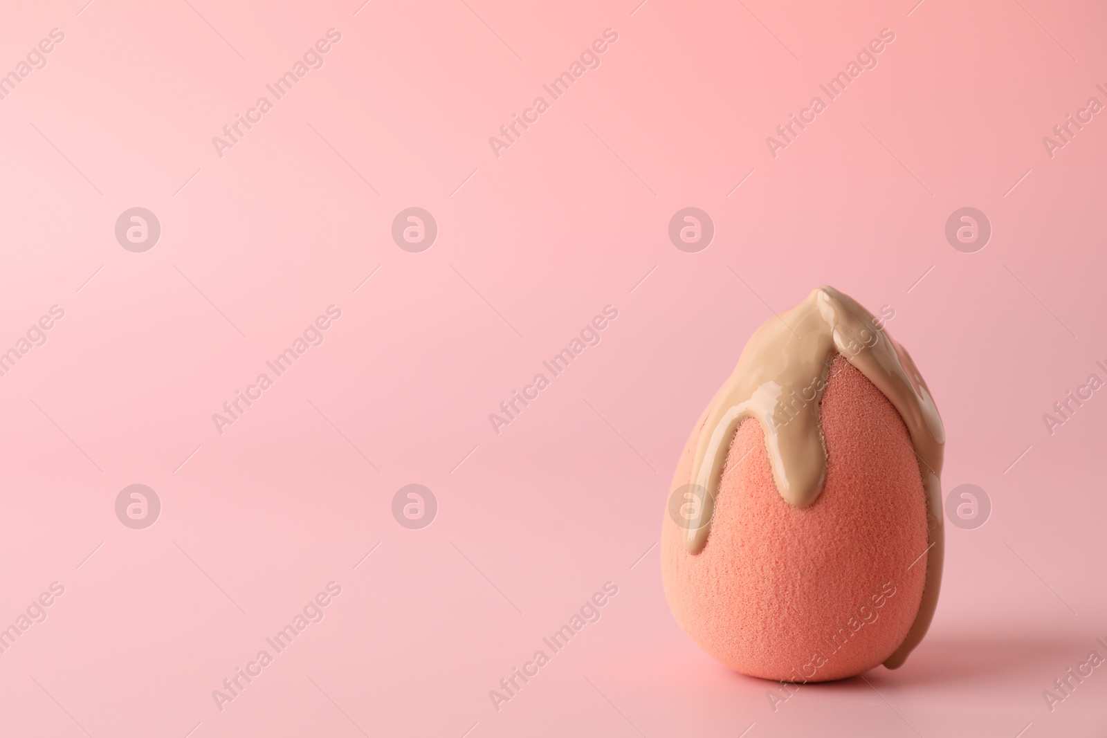 Photo of Makeup sponge with skin foundation on pink background, space for text