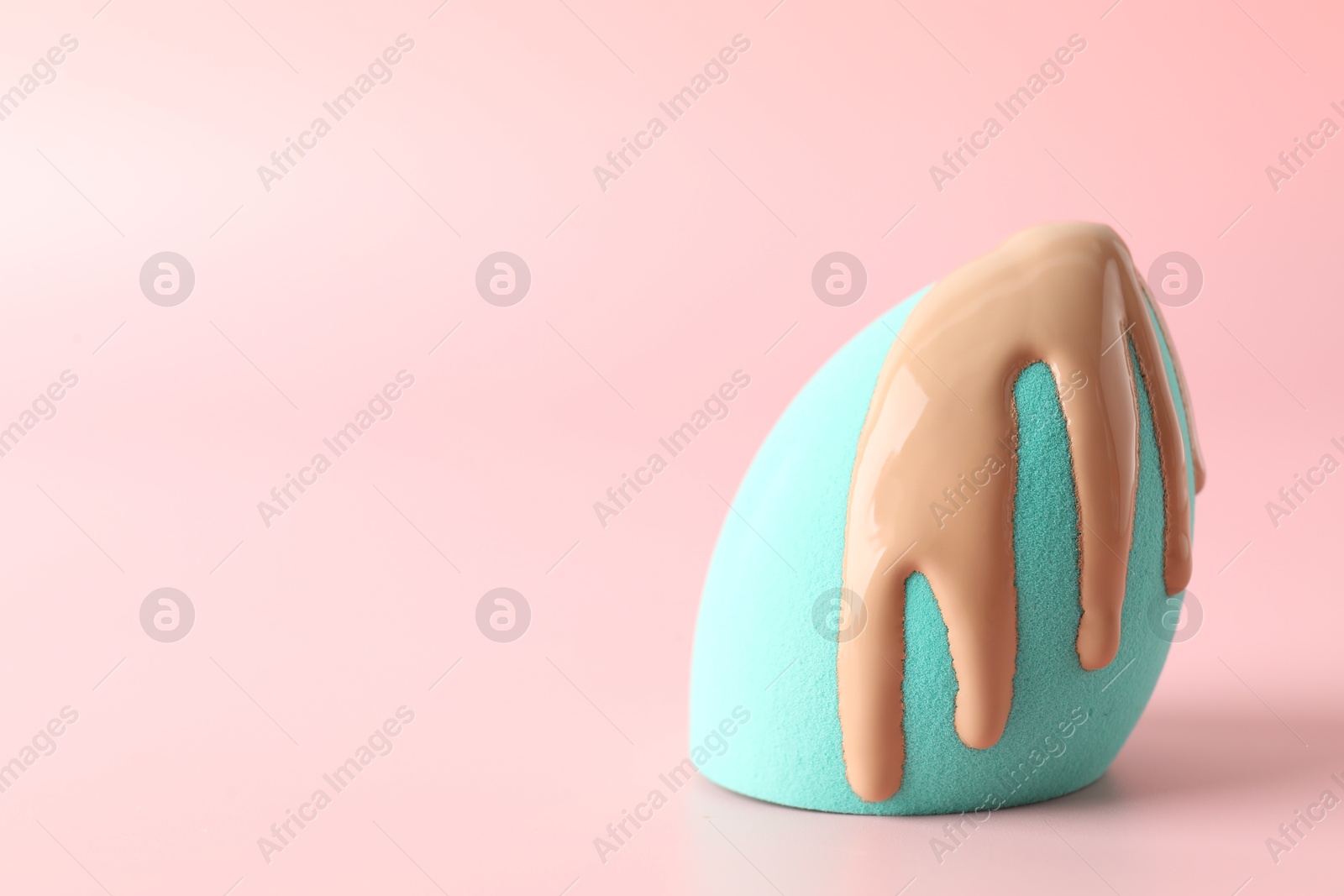 Photo of Makeup sponge with skin foundation on pink background, space for text