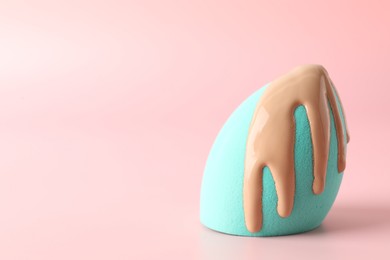 Makeup sponge with skin foundation on pink background, space for text