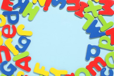 Photo of Learning alphabet. Frame made of magnetic letters on light blue background, top view. Space for text