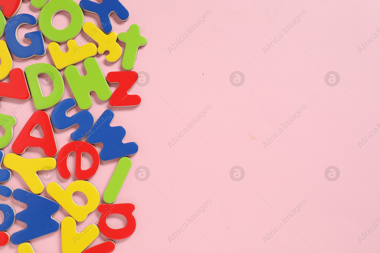 Photo of Learning alphabet. Magnetic letters on pink background, flat lay. Space for text