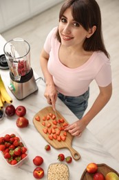 Photo of Young woman making delicious smoothie with blender at white marble table in kitchen, above view