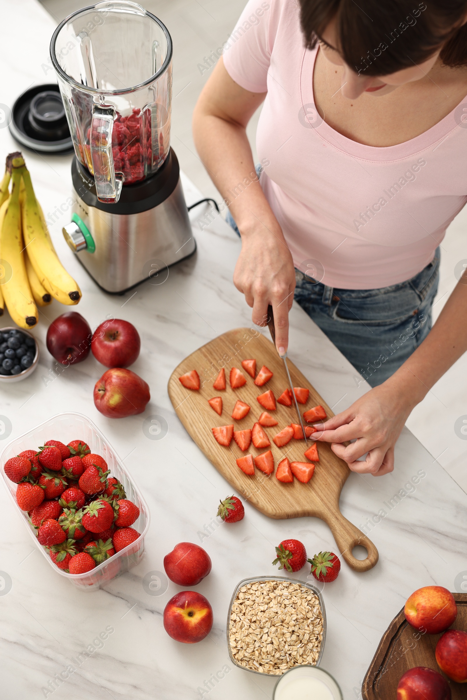 Photo of Woman making delicious smoothie with blender at white marble table in kitchen, above view