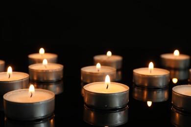 Photo of Many burning tealight candles on mirror surface against black background