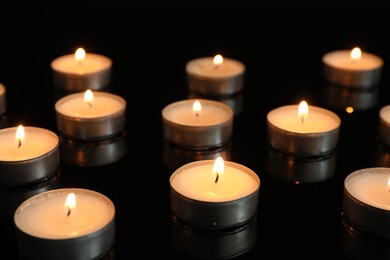 Photo of Many burning tealight candles on mirror surface against black background