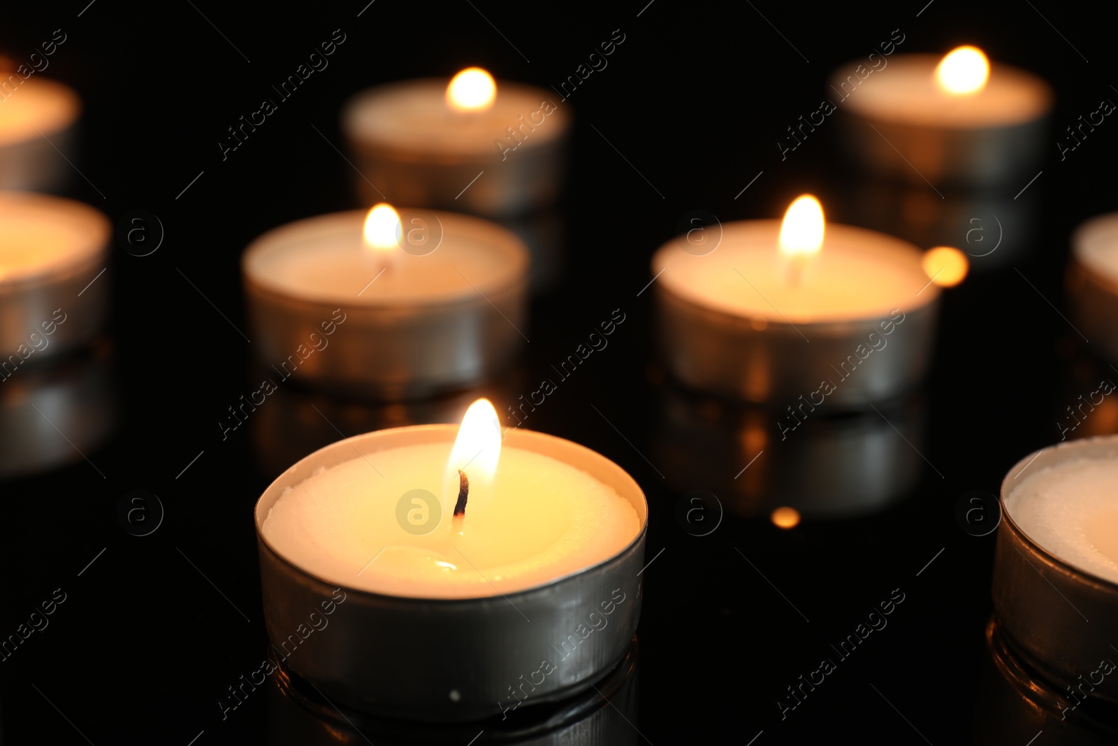 Photo of Many burning tealight candles on black background, closeup