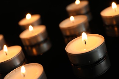 Many burning tealight candles on black background, closeup