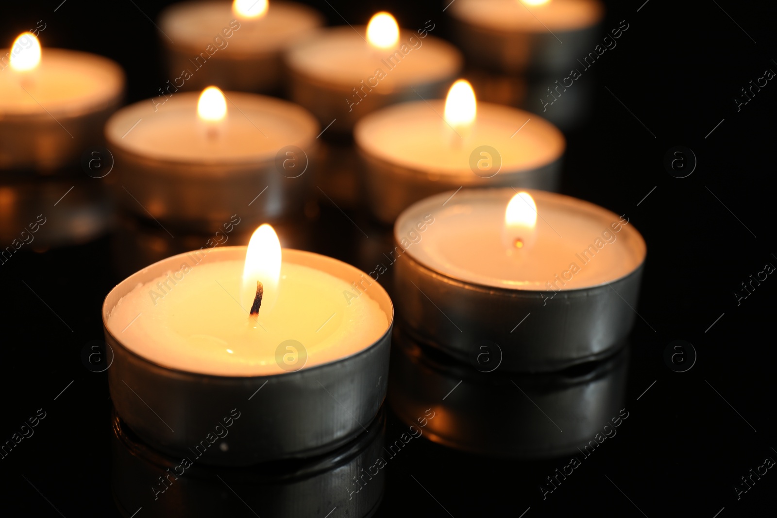 Photo of Many burning tealight candles on black background, closeup