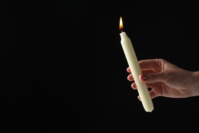 Photo of Woman holding burning candle on black background, closeup. Space for text