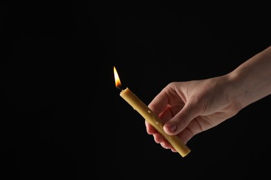 Woman holding burning church candle on black background, closeup