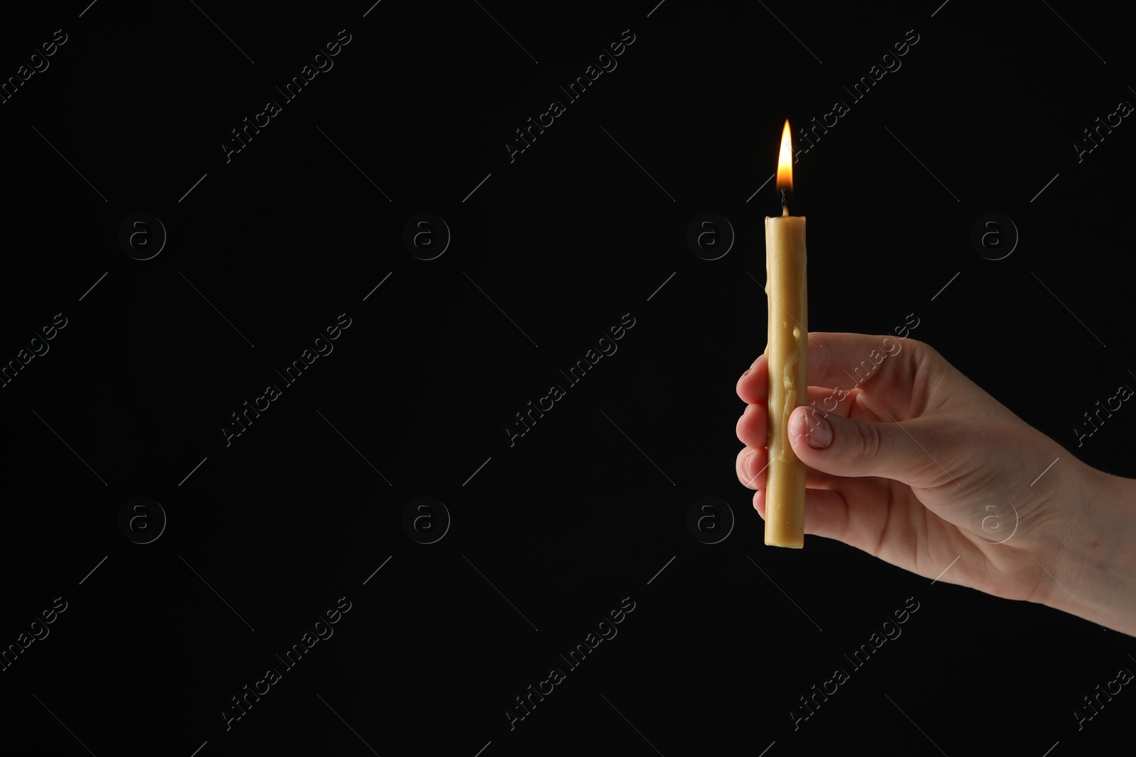 Photo of Woman holding burning church candle on black background, closeup. Space for text