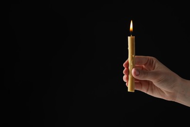 Woman holding burning church candle on black background, closeup. Space for text